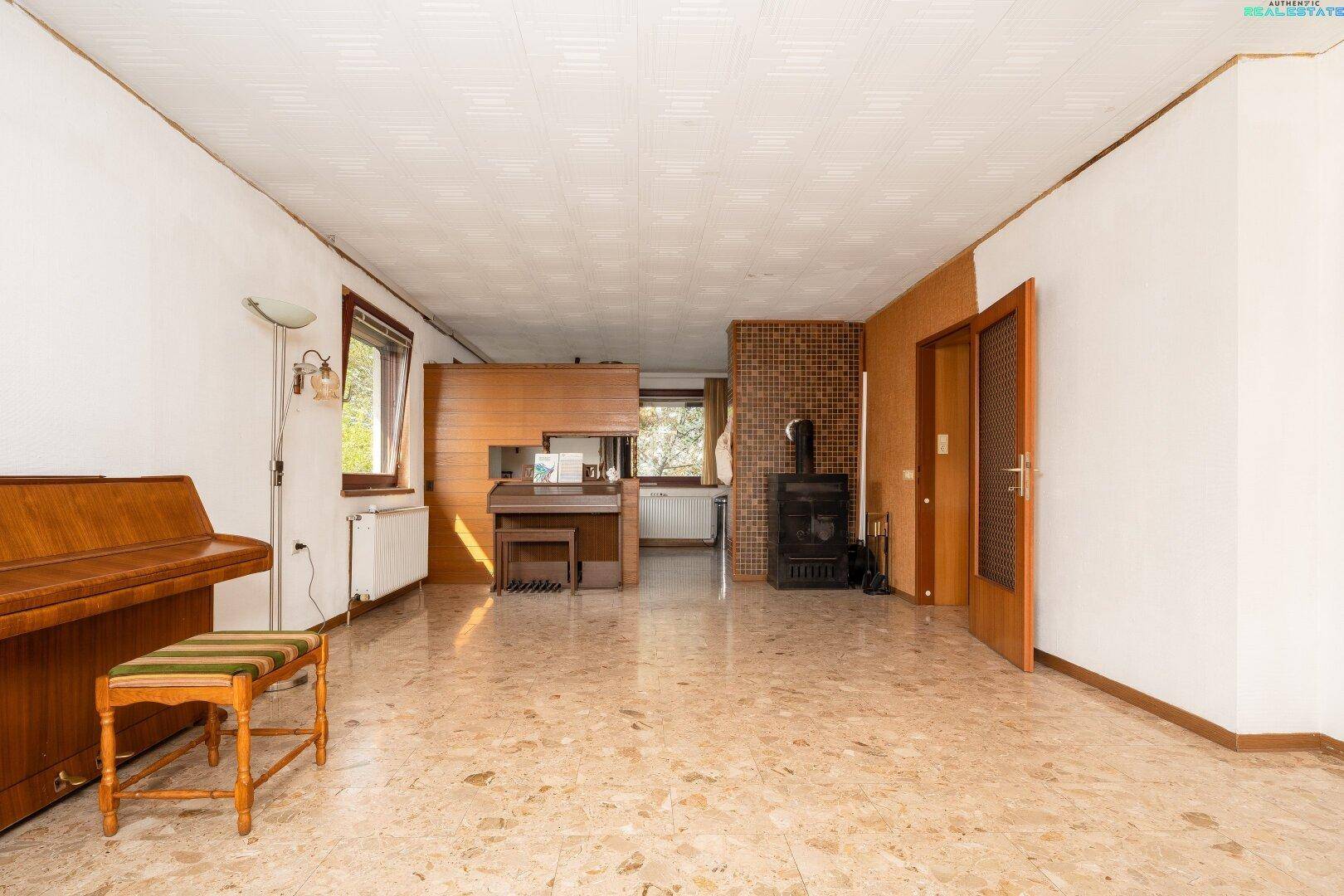 Geräumiges Wohnzimmer mit Steinboden, Kaminofen und einem Klavier, ideal für gesellige Abende.