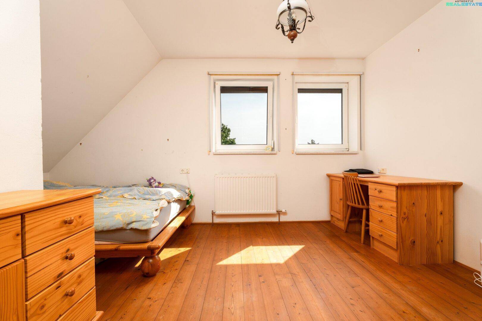 Schlafzimmer im Dachgeschoss mit Holzboden und zwei Fenstern, bietet viel natürliches Licht.
