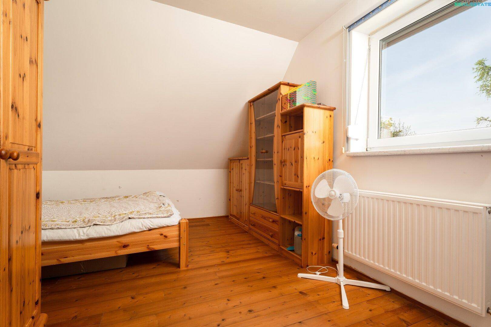 Helles Schlafzimmer im Dachgeschoss mit Holzboden, Fenster und einem Ventilator für Komfort.