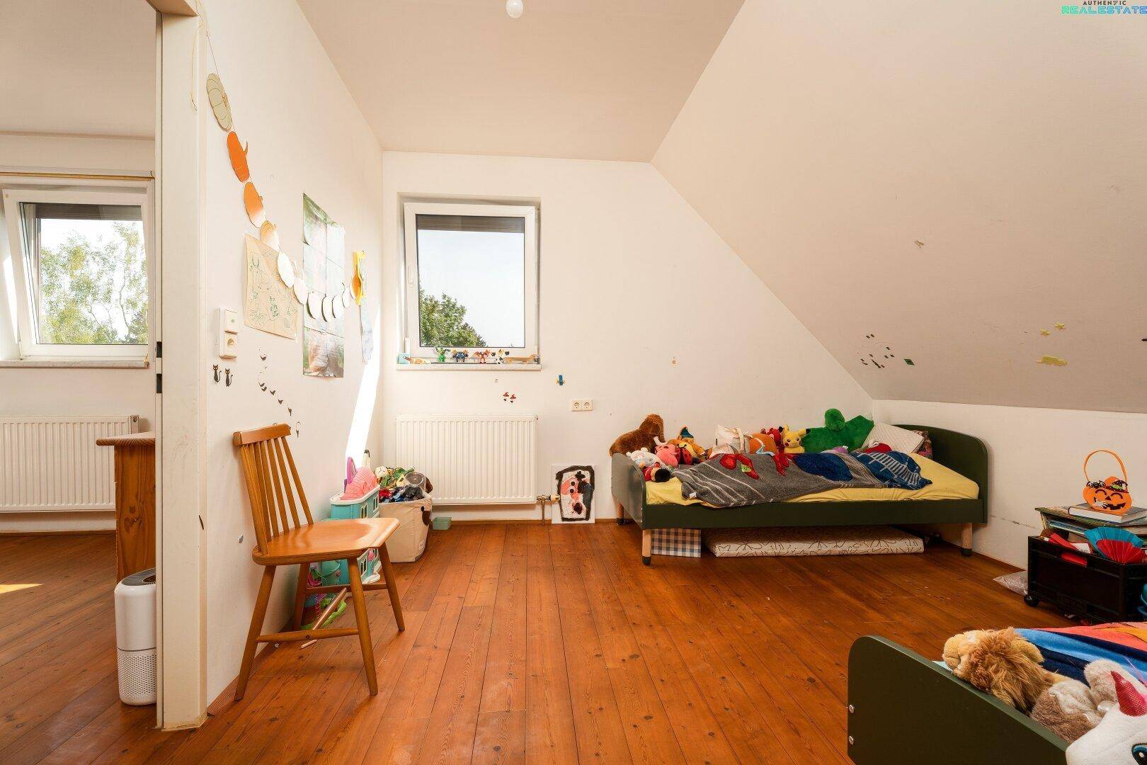 Kinderzimmer im Dachgeschoss mit Holzboden, Spielzeug und einem Fenster für Tageslicht.