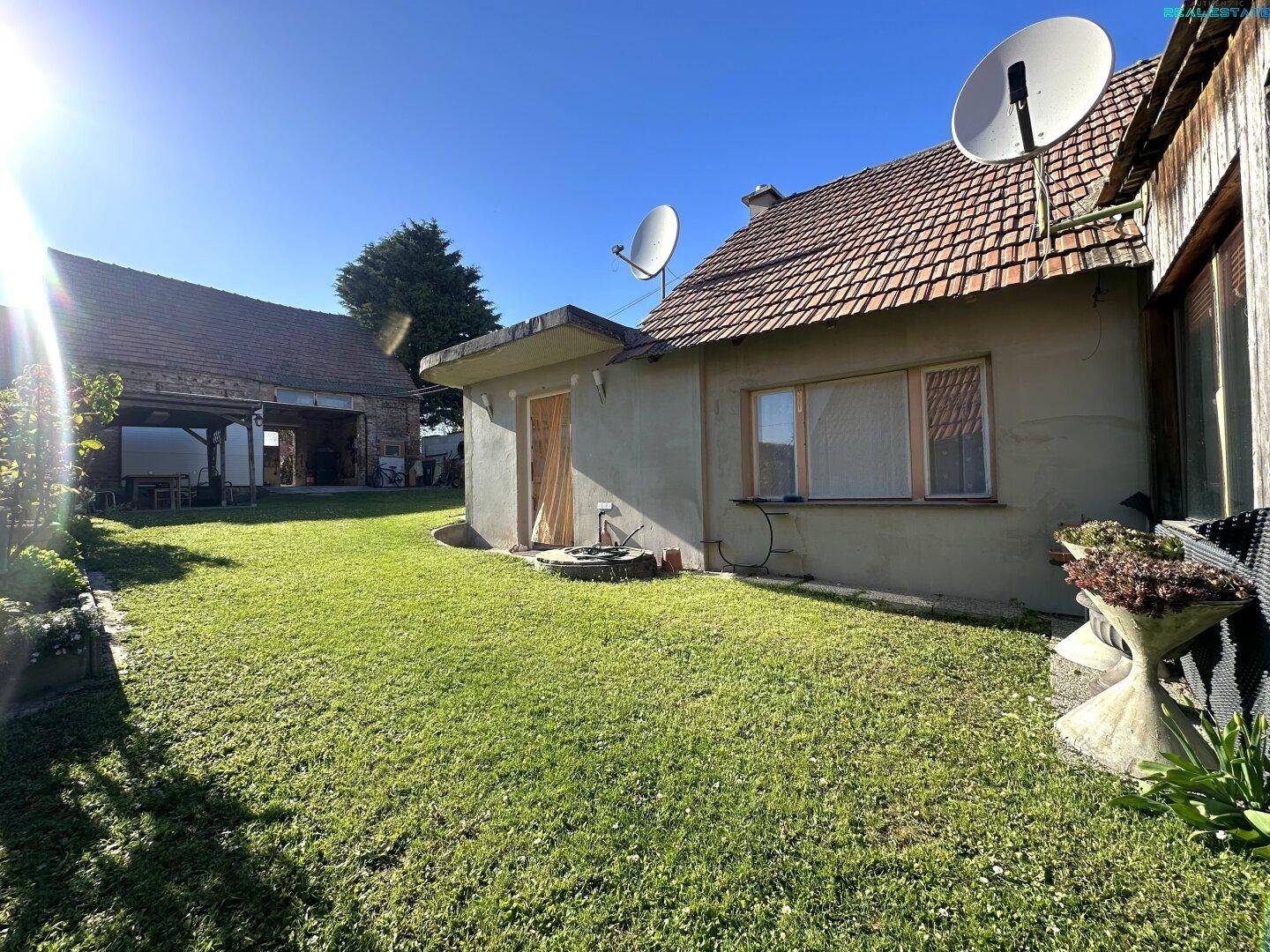 Sonnige Rasenfläche im Garten hinter dem Haus mit Satellitenschüsseln auf dem Dach.