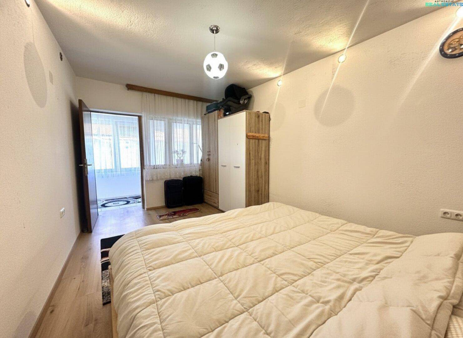 Helles Schlafzimmer mit Holzboden, Kleiderschrank und Zugang zu einem verglasten Balkon.