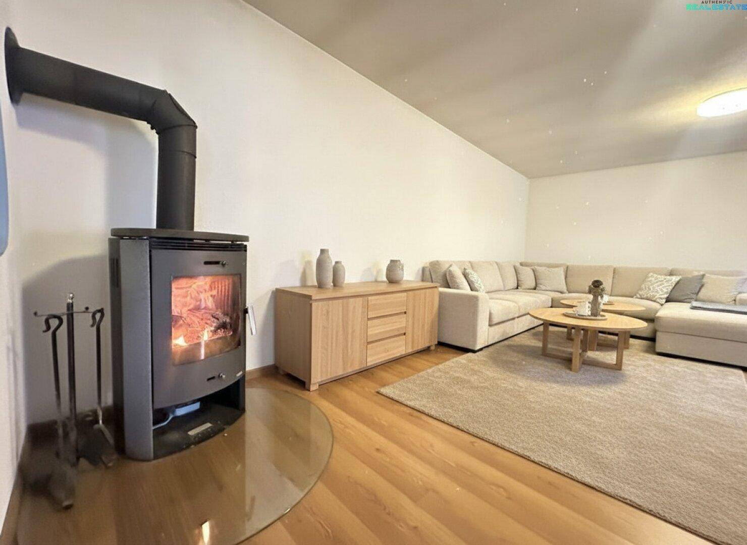 Modern eingerichtetes Wohnzimmer mit Kaminofen, hellem Sofa und Holzboden.