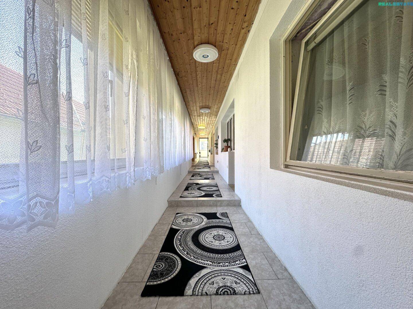 Langer Flur mit Fliesenboden, Holzdecke und Fenstern, die viel Licht hereinlassen.