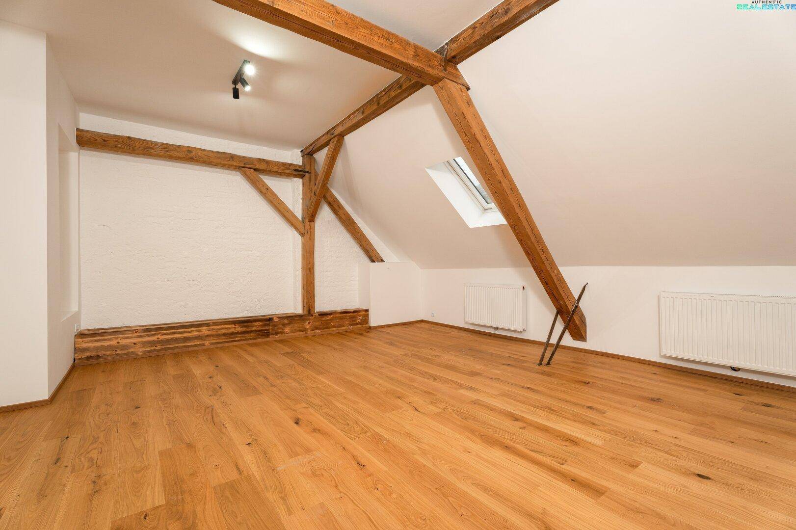 Ausgebautes Dachgeschoss mit sichtbaren Holzbalken, Parkettboden und Dachfenster.