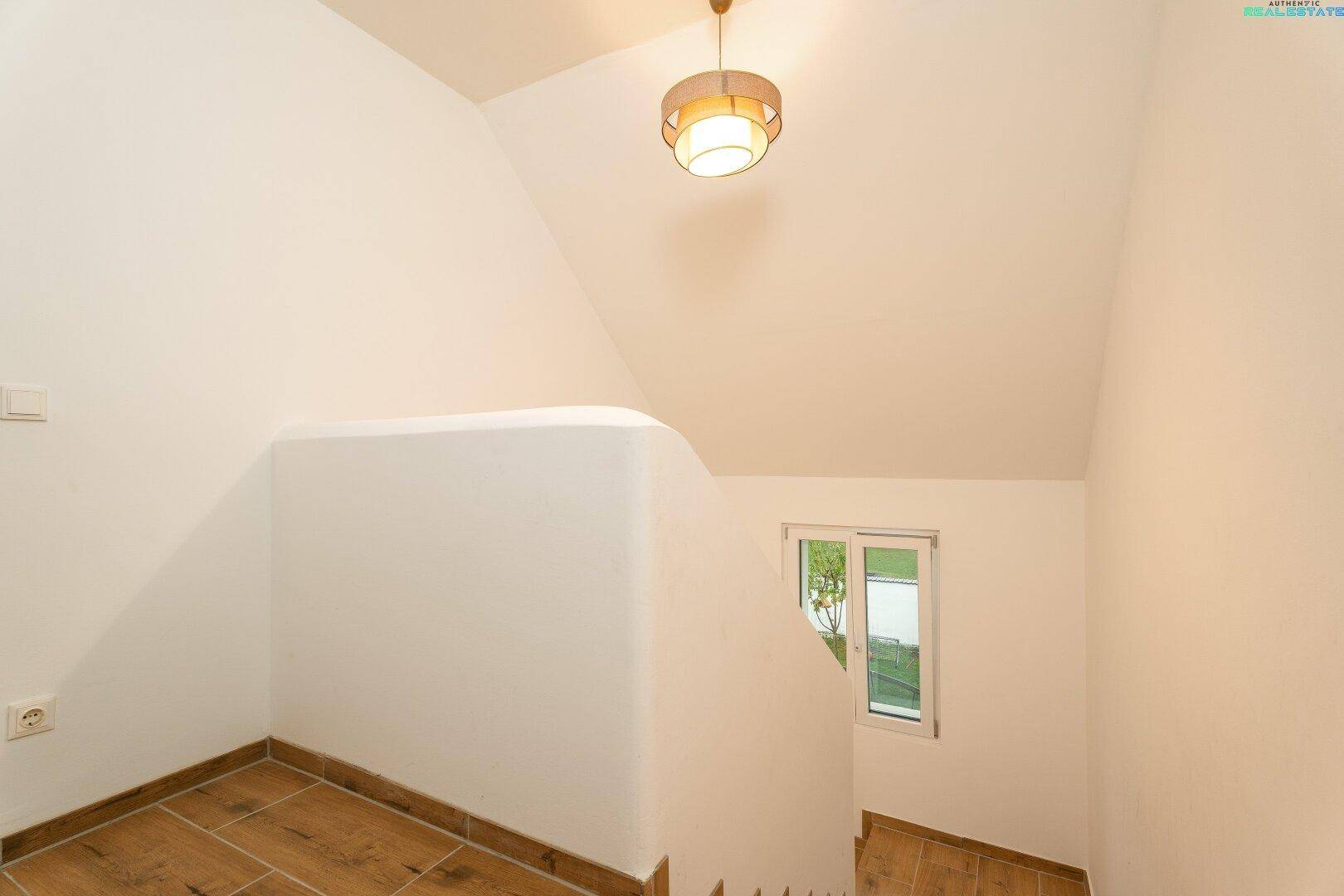 Heller Treppenaufgang mit Holzstufen und weiß gestrichenen Wänden.