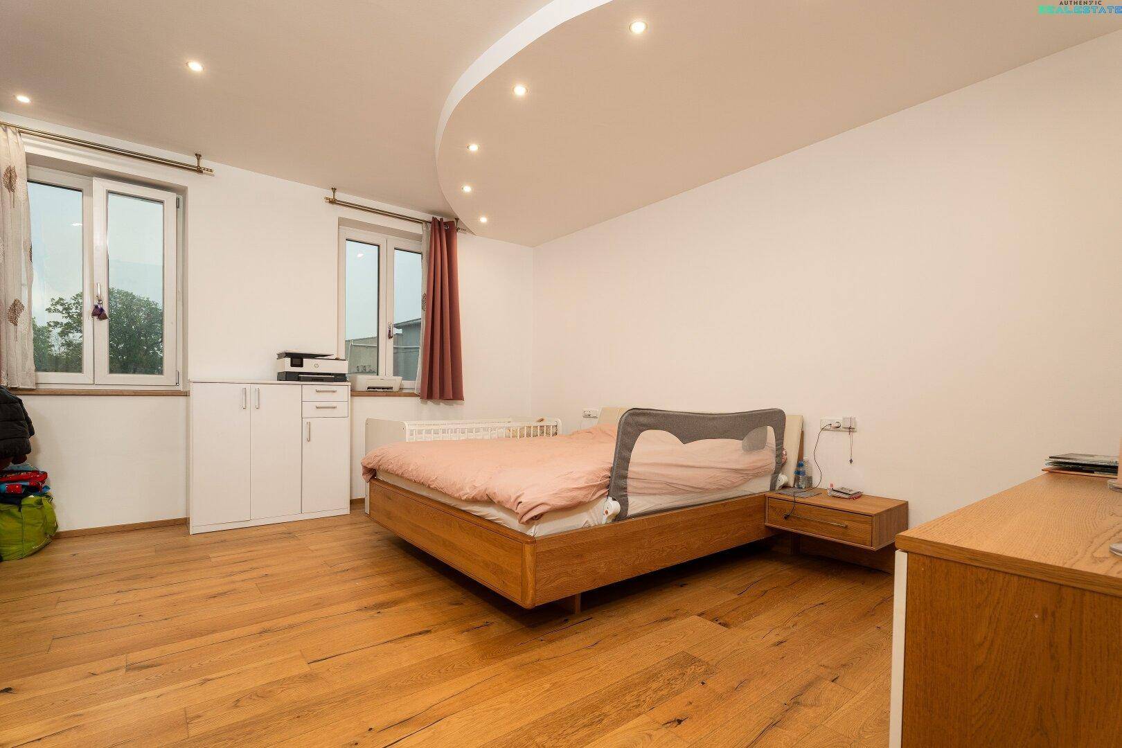 Helles Schlafzimmer mit Holzbett, Parkettboden und Einbaustrahlern in der Decke.