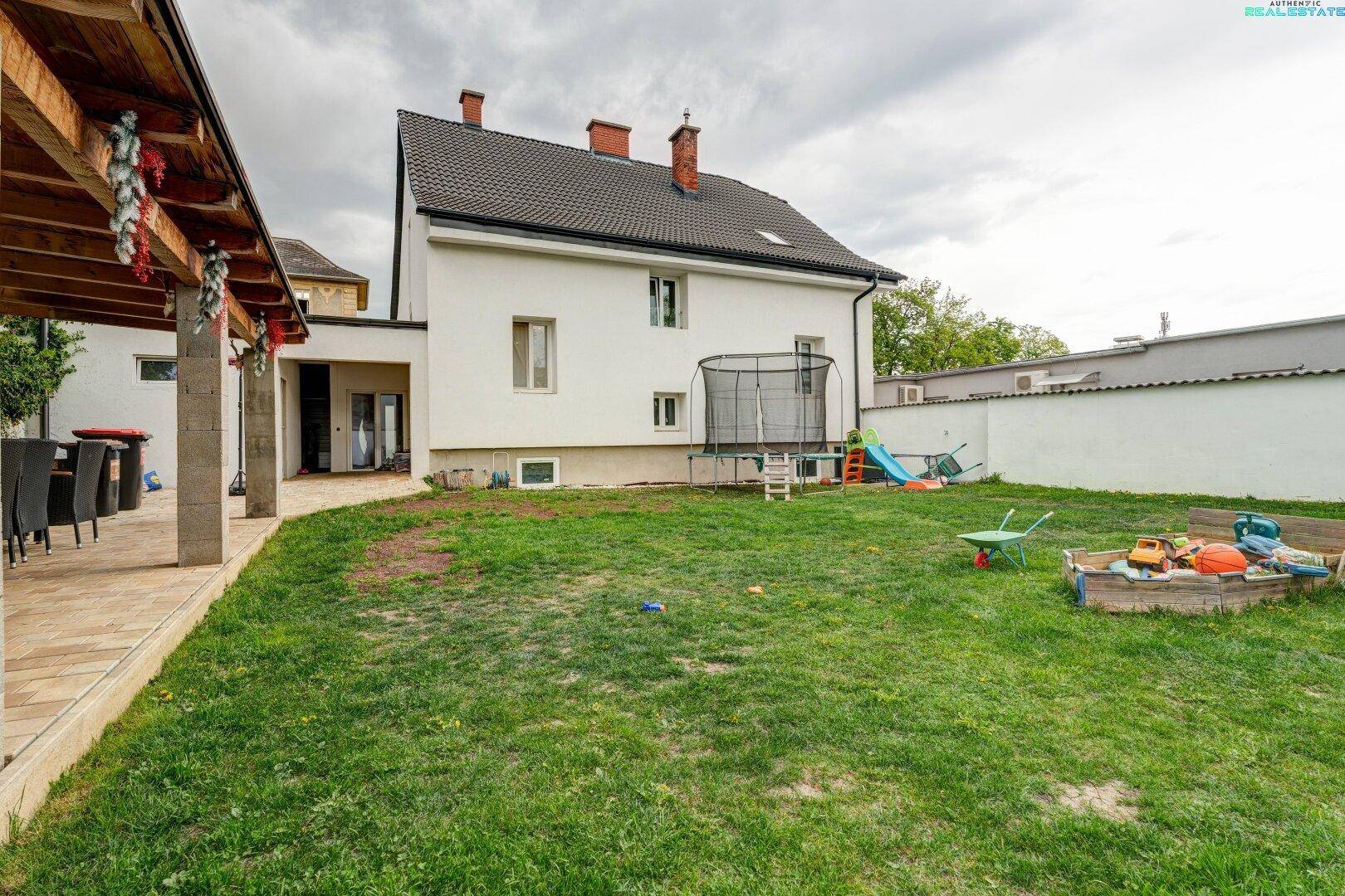 Hinterhof mit großem Rasen, Trampolin und überdachtem Terrassenbereich am Haus.
