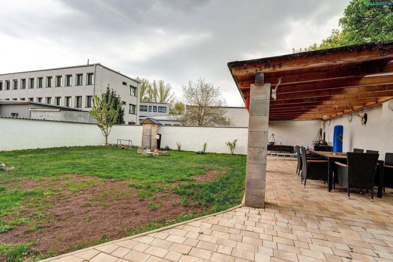 Gepflasterte Terrasse und Rasenfläche im Garten mit Blick auf umliegende Gebäude.