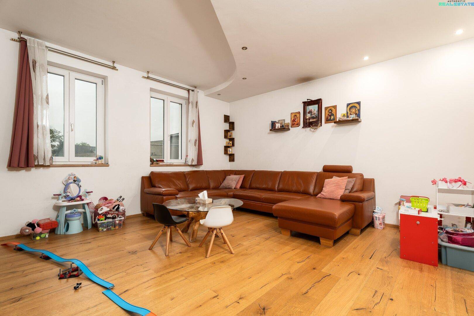 Gemütliches Wohnzimmer mit großem Ledersofa, Holzfußboden und viel Tageslicht.