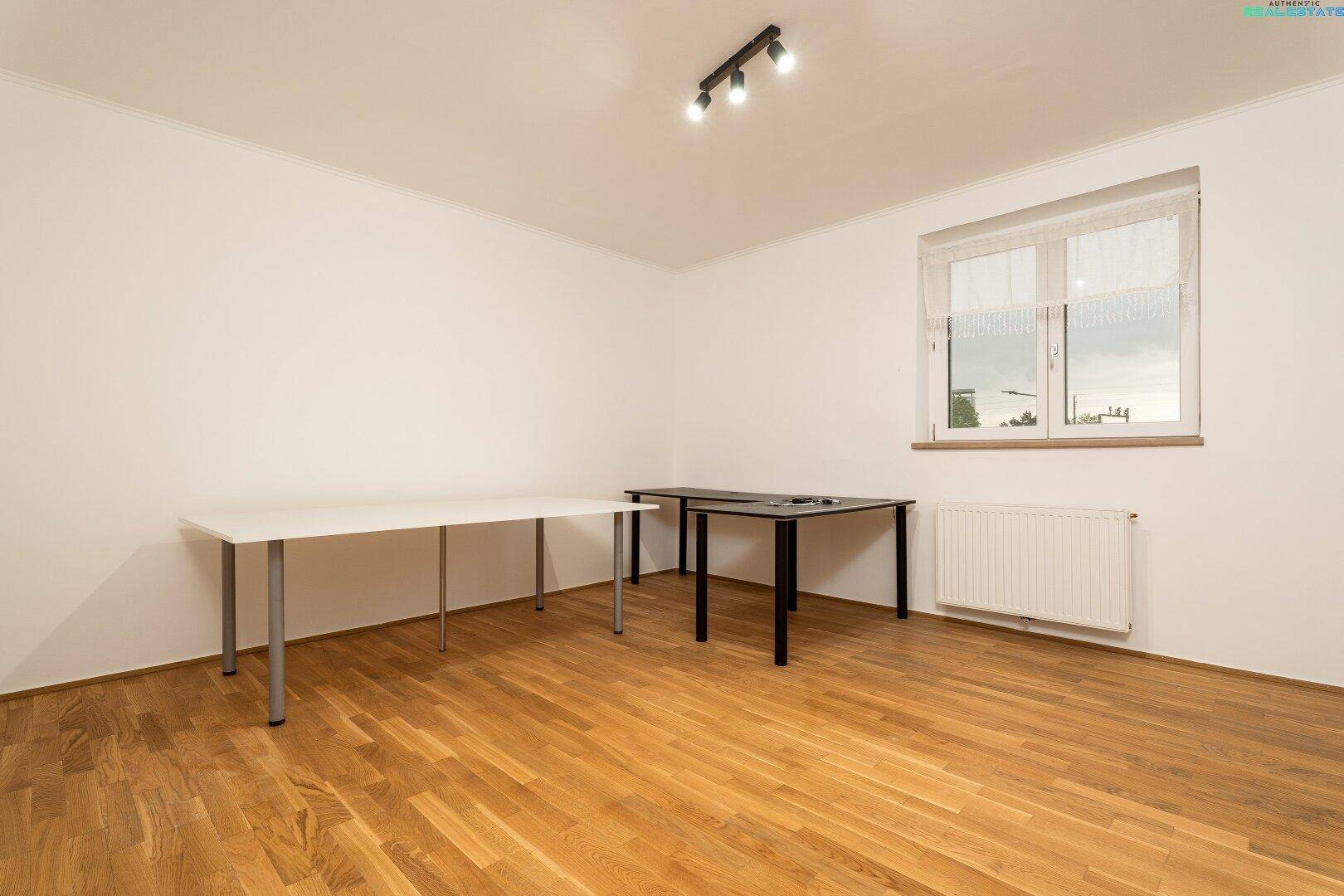 Helles Zimmer mit Holzfußboden, großem Fenster und zwei Arbeitstischen.