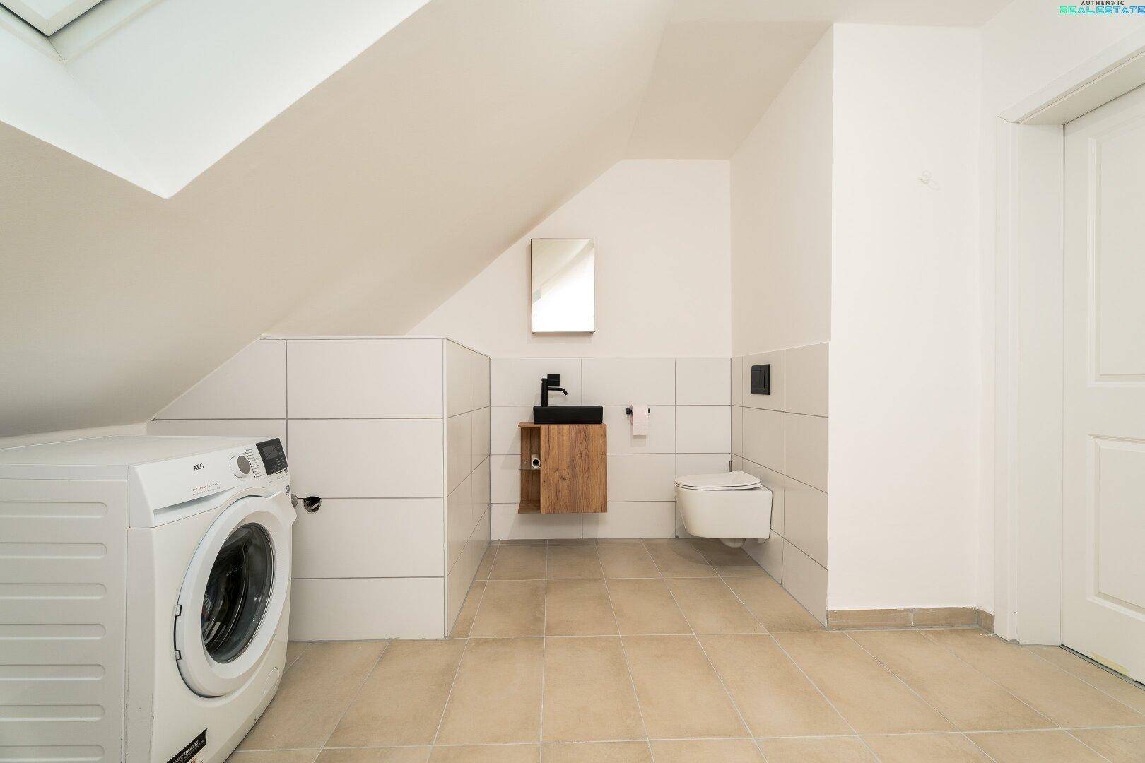 Funktionelles Dachgeschossbad mit Toilette, Waschbecken und Waschmaschine.