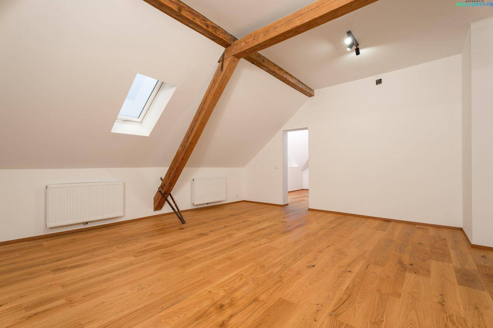Geräumiges Dachgeschoss mit Holzbalken, Parkettboden und Zugang zu weiteren Räumen.