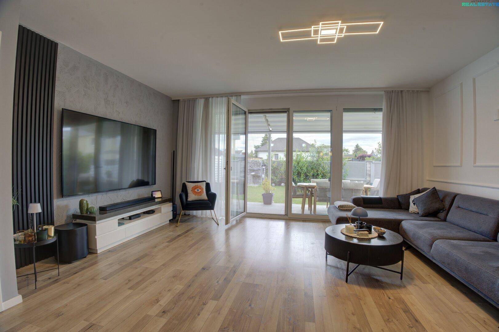 Geräumiges Wohnzimmer mit Holzboden, großem Fernseher und Zugang zur sonnigen Terrasse.