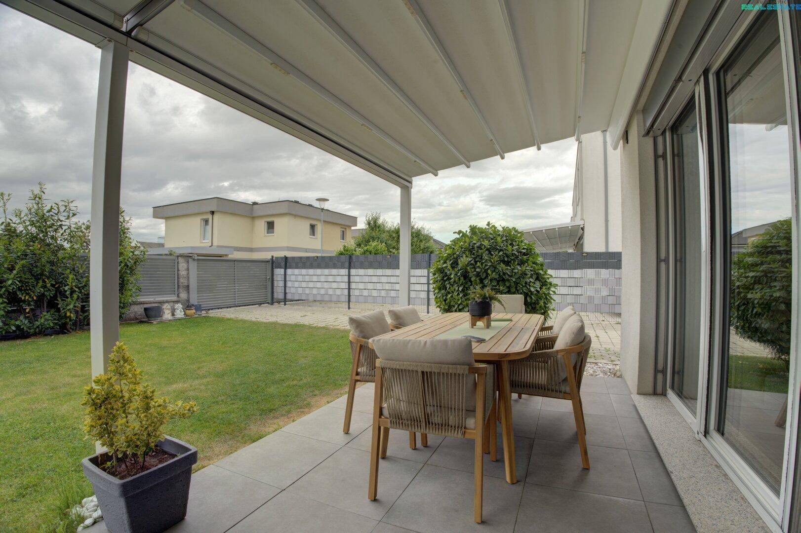 Überdachte Terrasse mit Gartenmöbeln und Blick auf den gepflegten Rasenbereich.