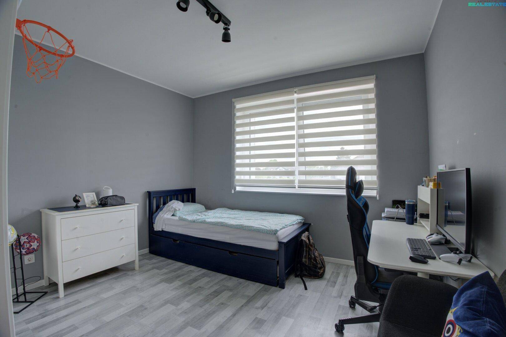Kinderzimmer mit Einzelbett, Schreibtisch und hellem Laminatboden, ideal zum Spielen und Lernen.
