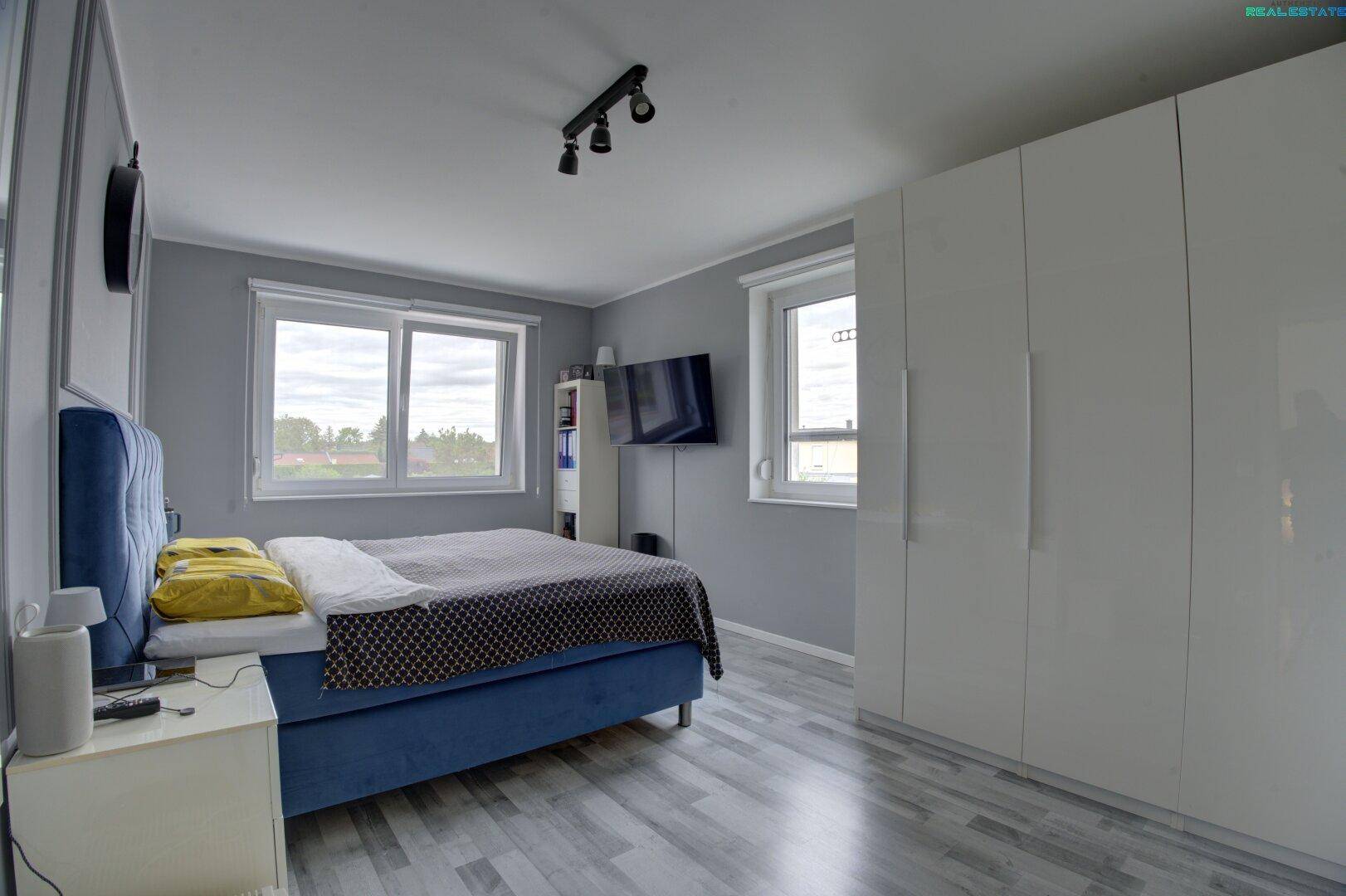Geräumiges Schlafzimmer mit Doppelbett, großem Kleiderschrank und hellen Fenstern.