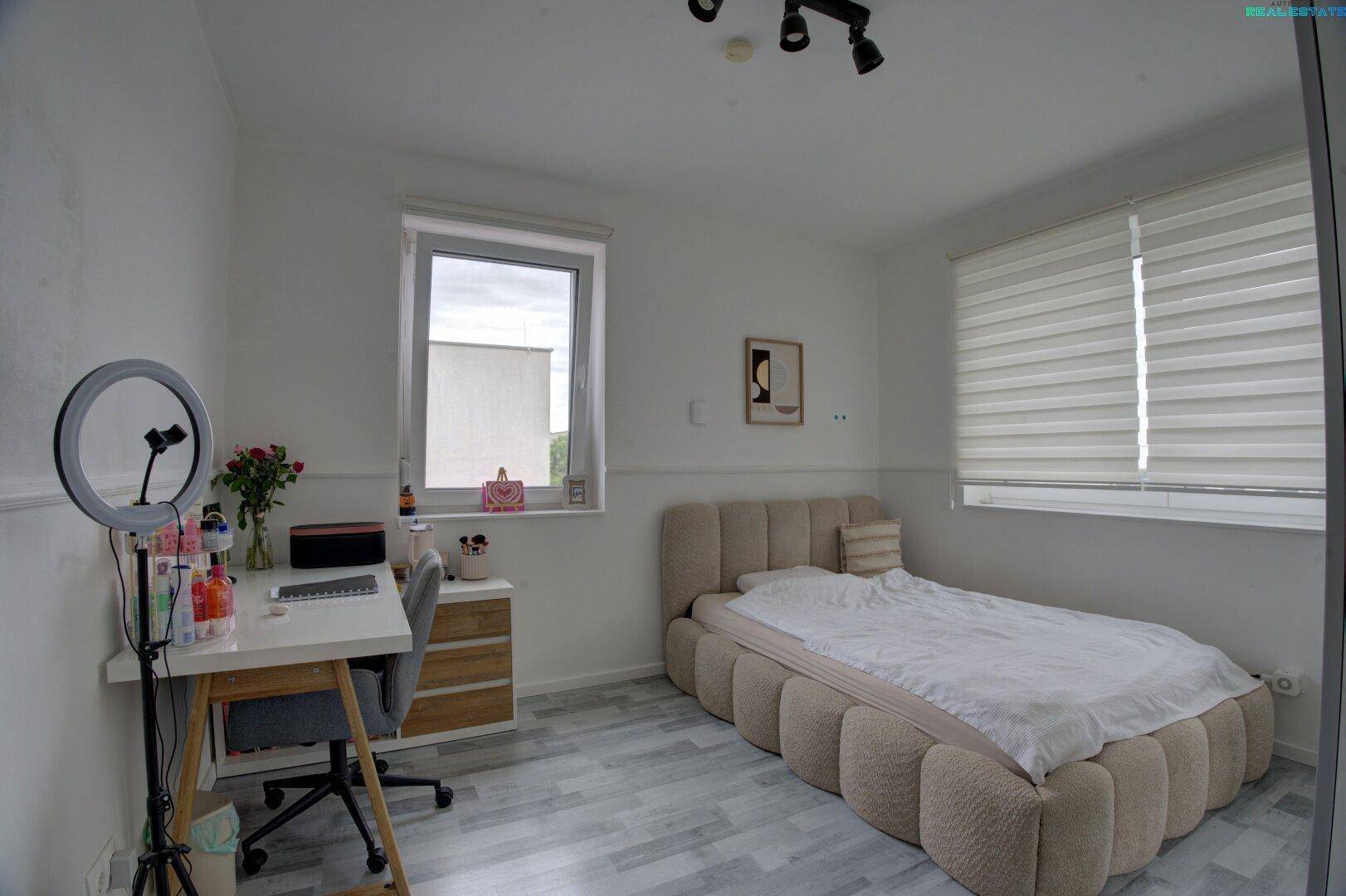 Helles Schlafzimmer mit modernem Bett, Schreibtisch und großem Fenster für viel Tageslicht.