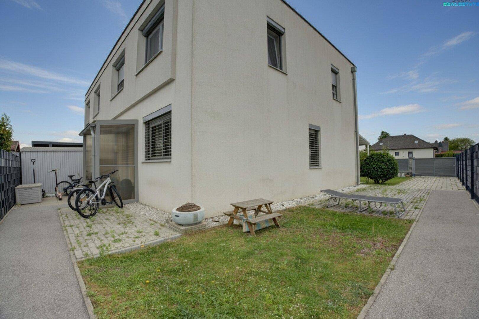 Seitenansicht des Hauses mit kleinem Rasenbereich, gepflastertem Weg und Abstellplatz für Fahrräder.