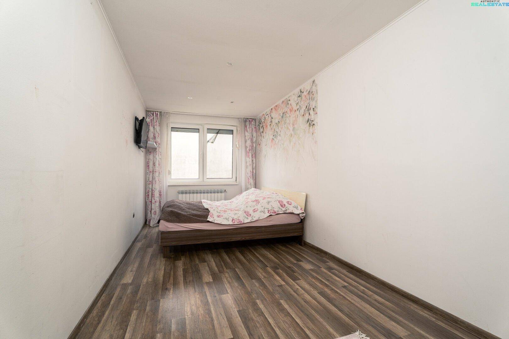 Schlafzimmer mit Holzboden, Fenster und floraler Akzentwand.