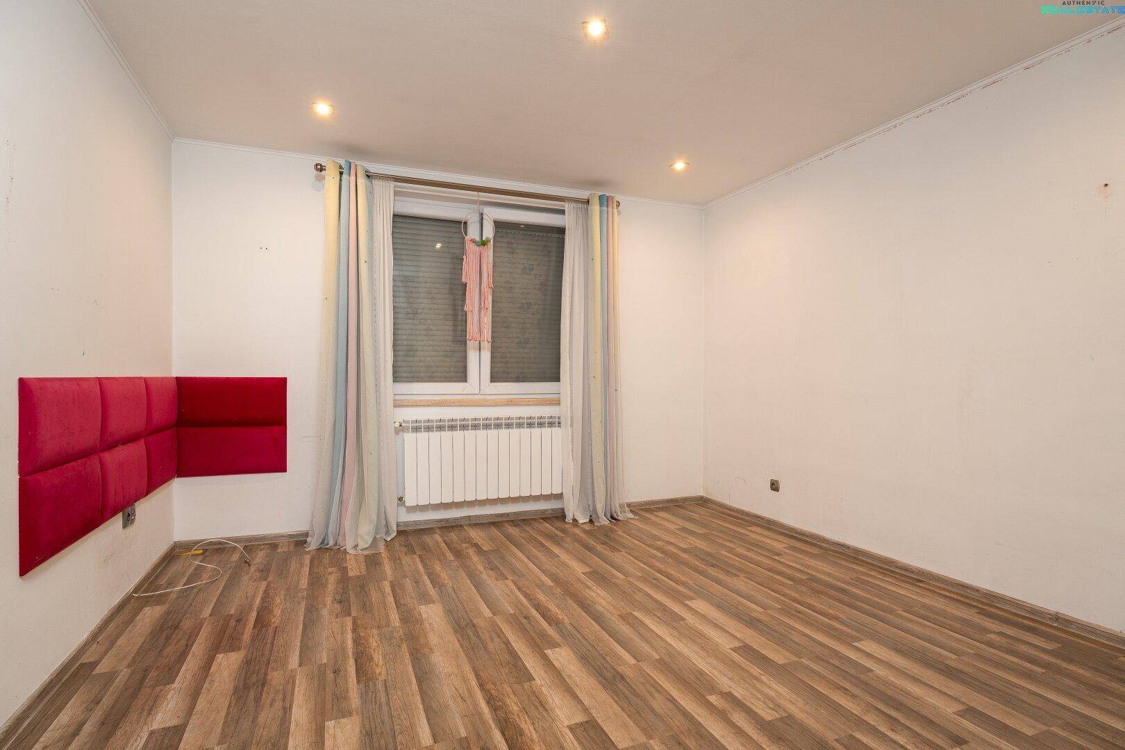 Schlafzimmer mit Holzboden, Fenster und roter Wandpolsterung.