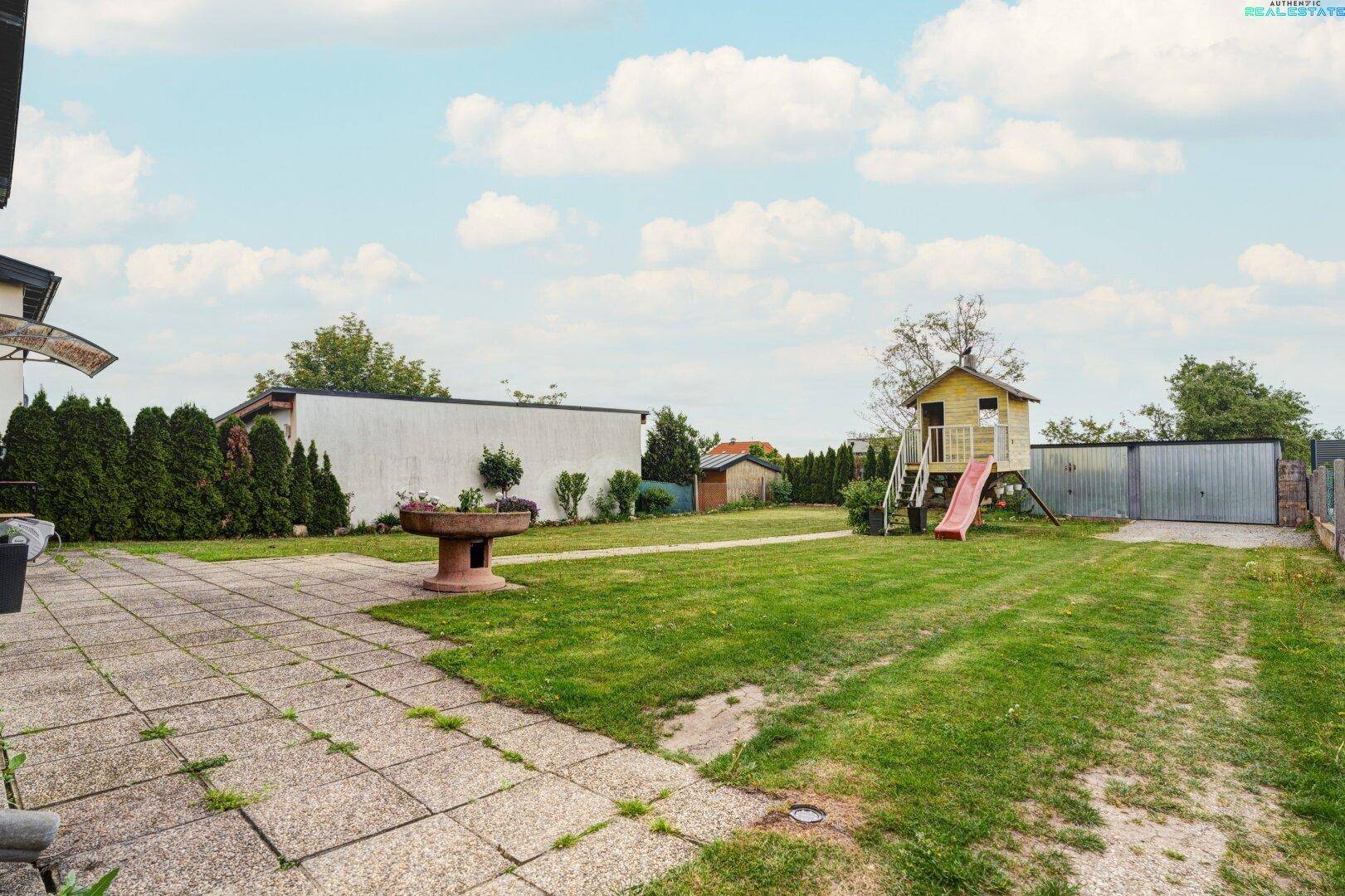 Großer Garten mit Terrasse, Rasenfläche und Kinderspielhaus.