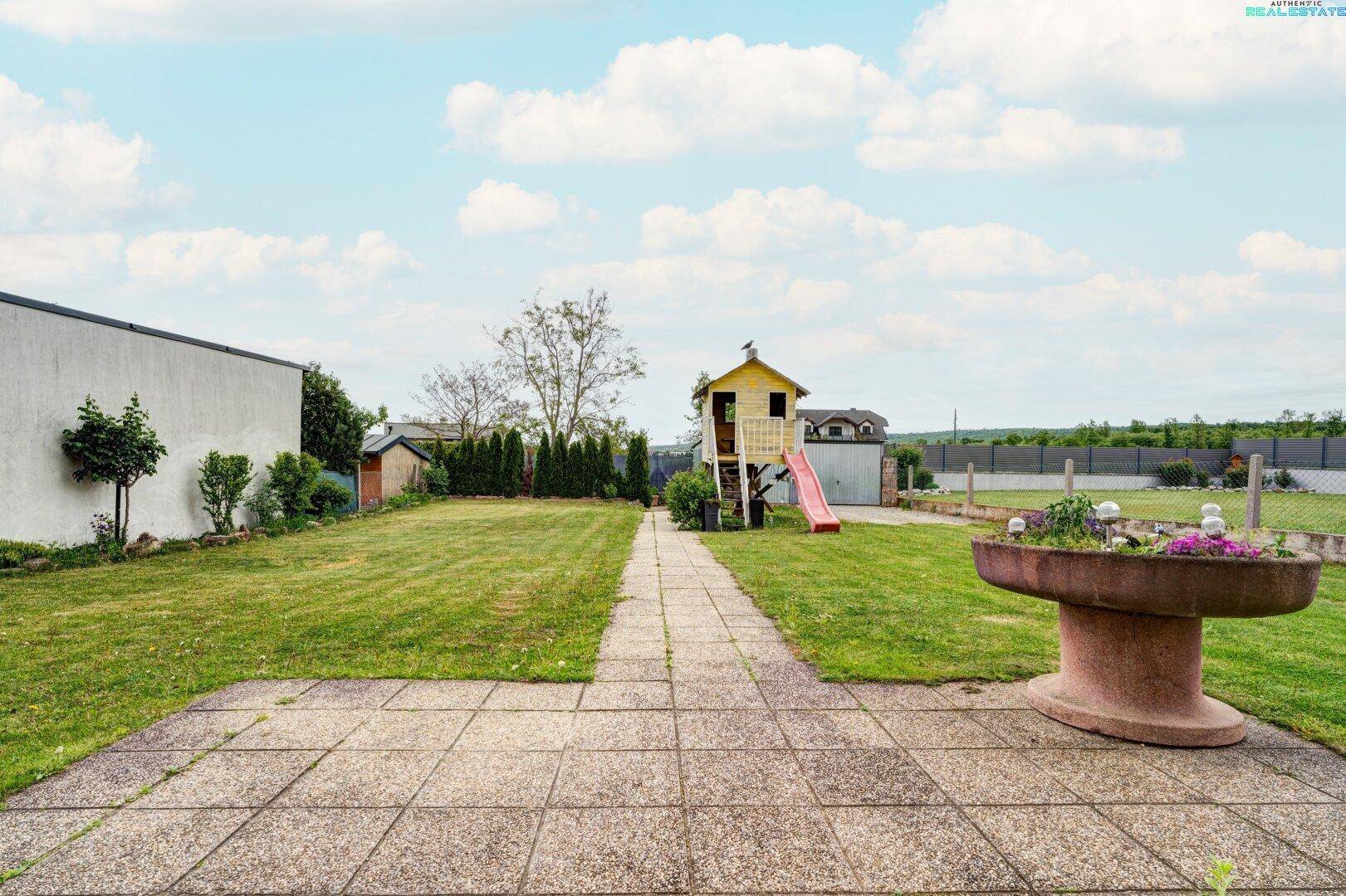 Gepflegter Garten mit Terrasse, Rasenweg und Kinderspielhaus.