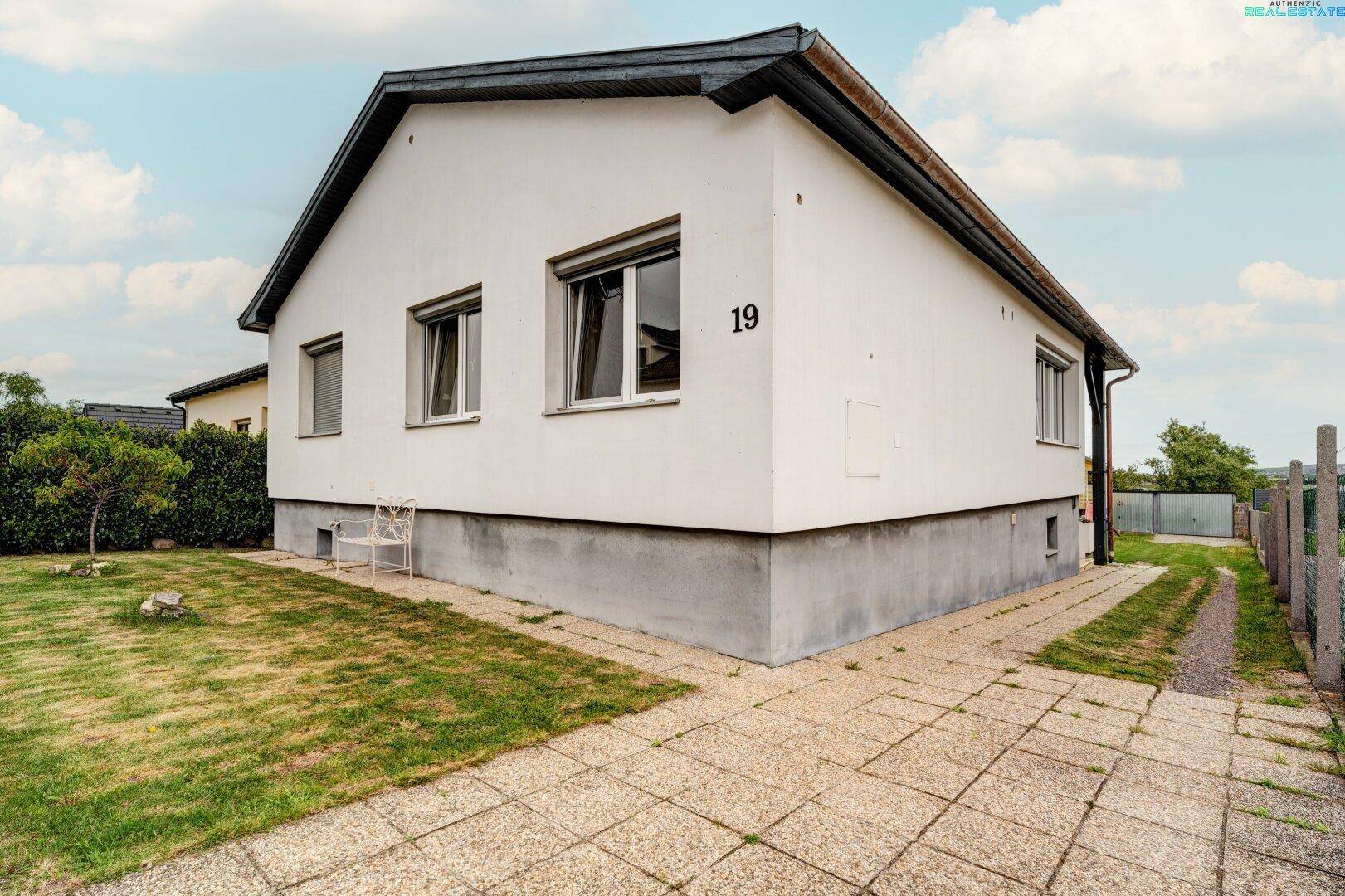Einfamilienhaus mit weißer Fassade, gepflastertem Weg und Garten.