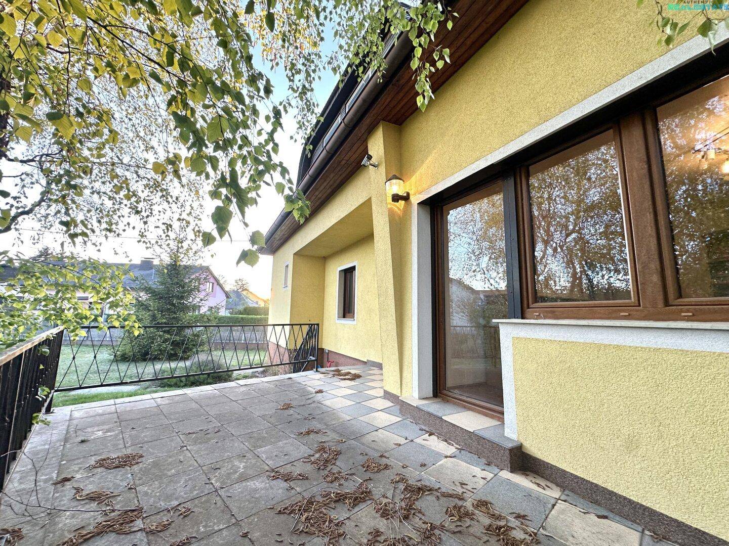 Geflieste Terrasse am Haus mit Blick ins Grüne und herbstlichem Laub auf dem Boden.