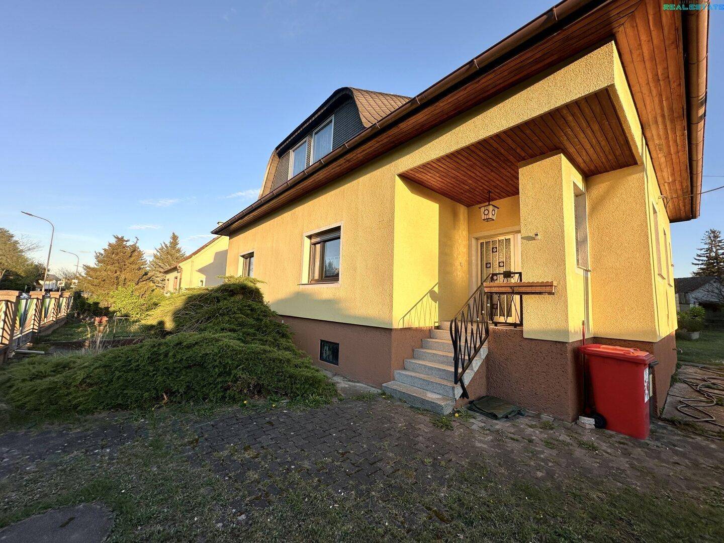 Eingangsbereich des gelben Hauses mit Treppe und überdachtem Vorbau.