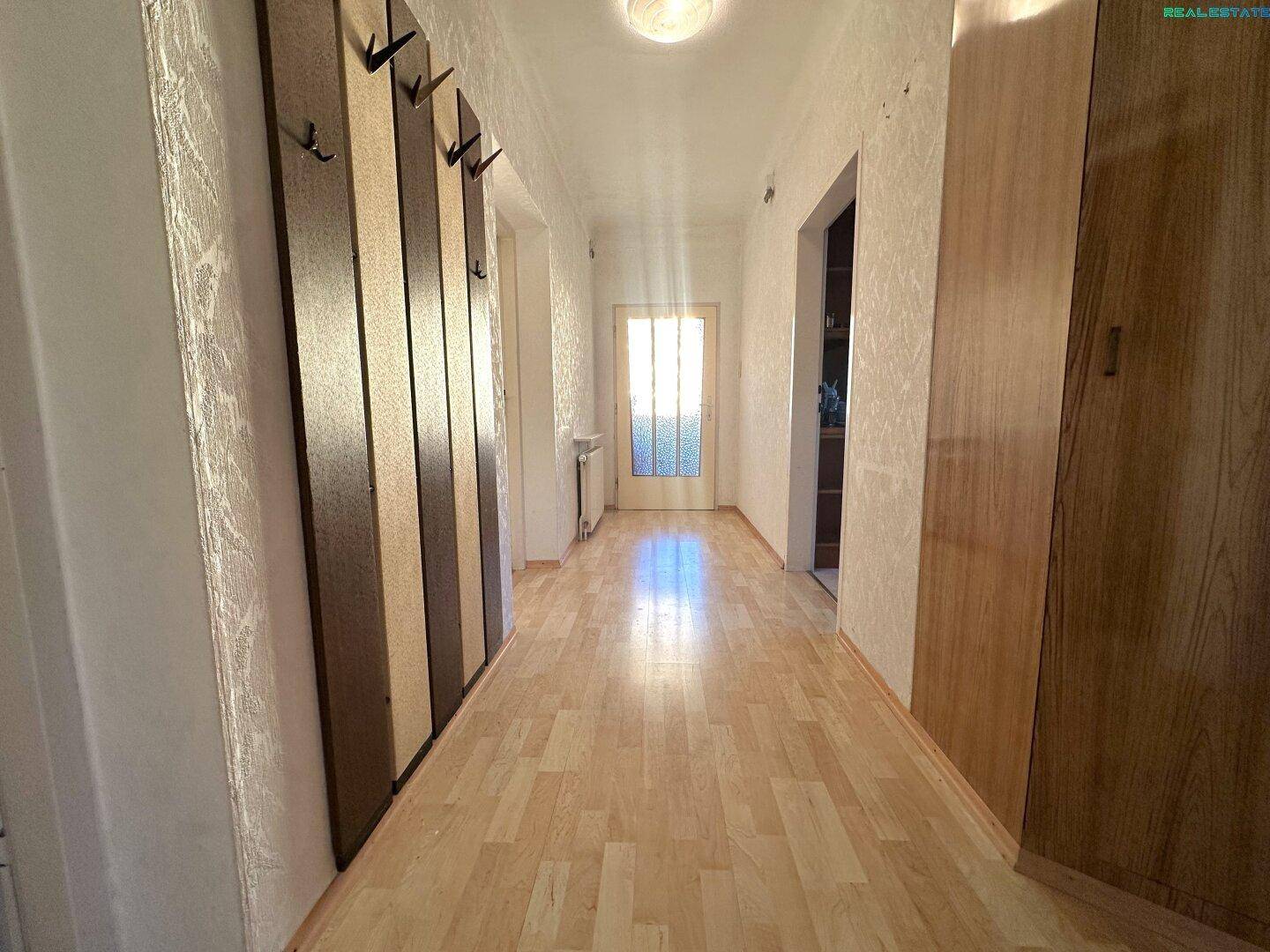Langer Flur mit Laminatboden, Garderobe und einer Tür mit Glaseinsatz am Ende.