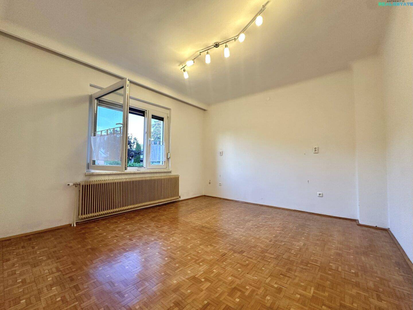 Geräumiges Zimmer mit Parkettboden, großem Fenster und Heizkörper, ideal als Wohn- oder Schlafzimmer.