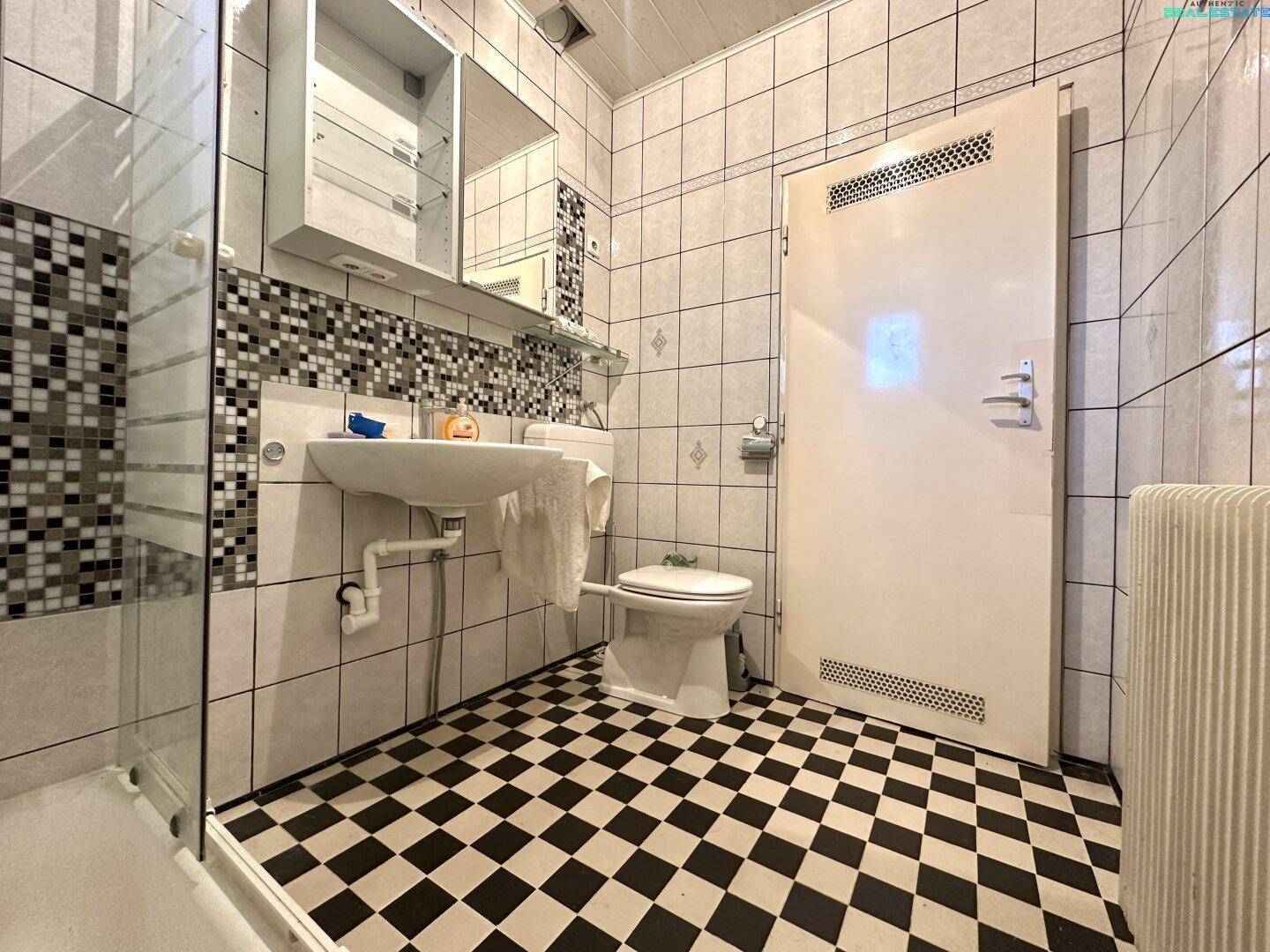 Badezimmer mit schwarz-weiß kariertem Fliesenboden, Waschbecken und Toilette.