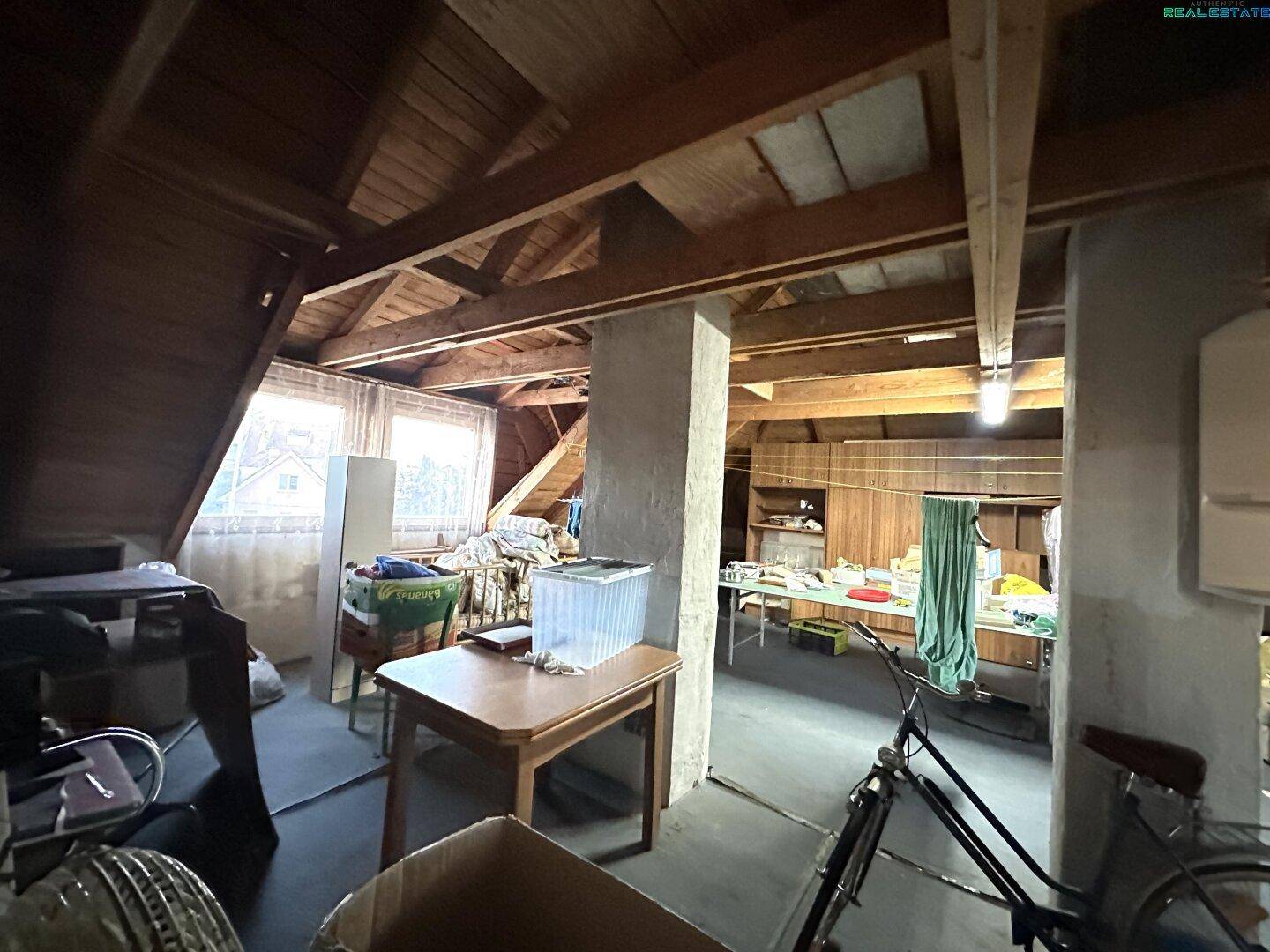 Unausgebauter Dachboden mit sichtbaren Holzbalken und Fenstern, bietet Ausbaupotenzial.