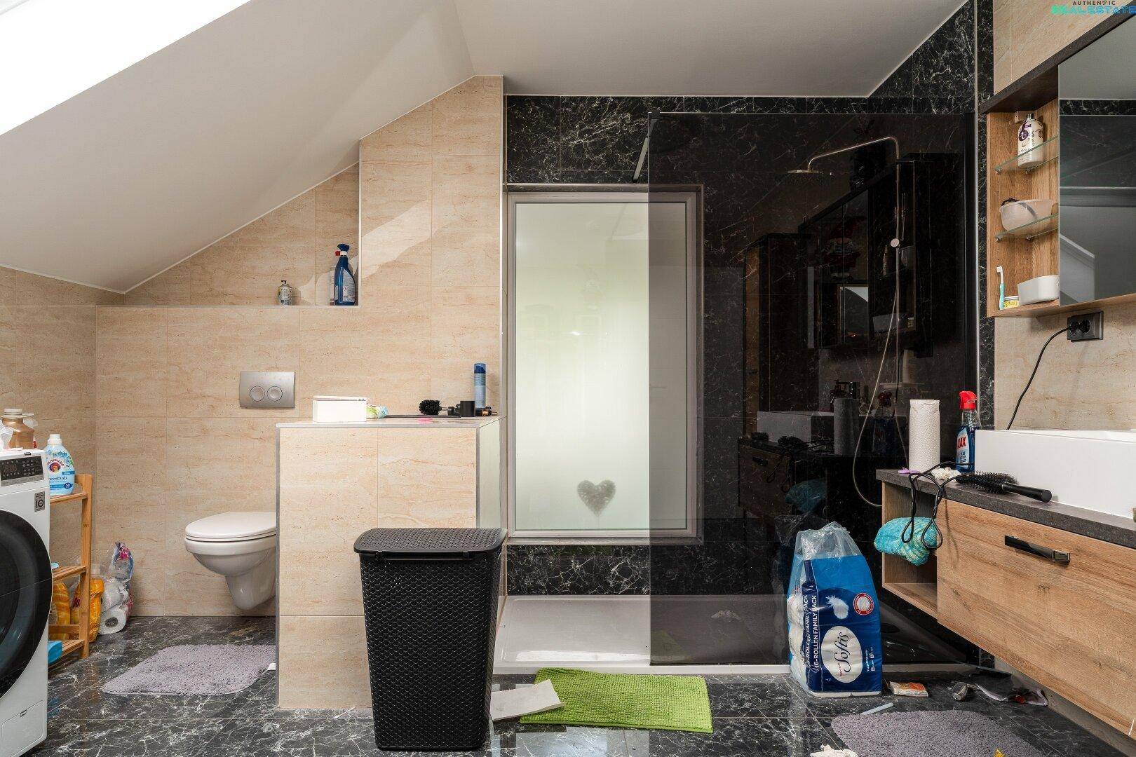 Badezimmer im Dachgeschoss mit Dusche, WC und dunklen Fliesen, modern und funktional gestaltet.