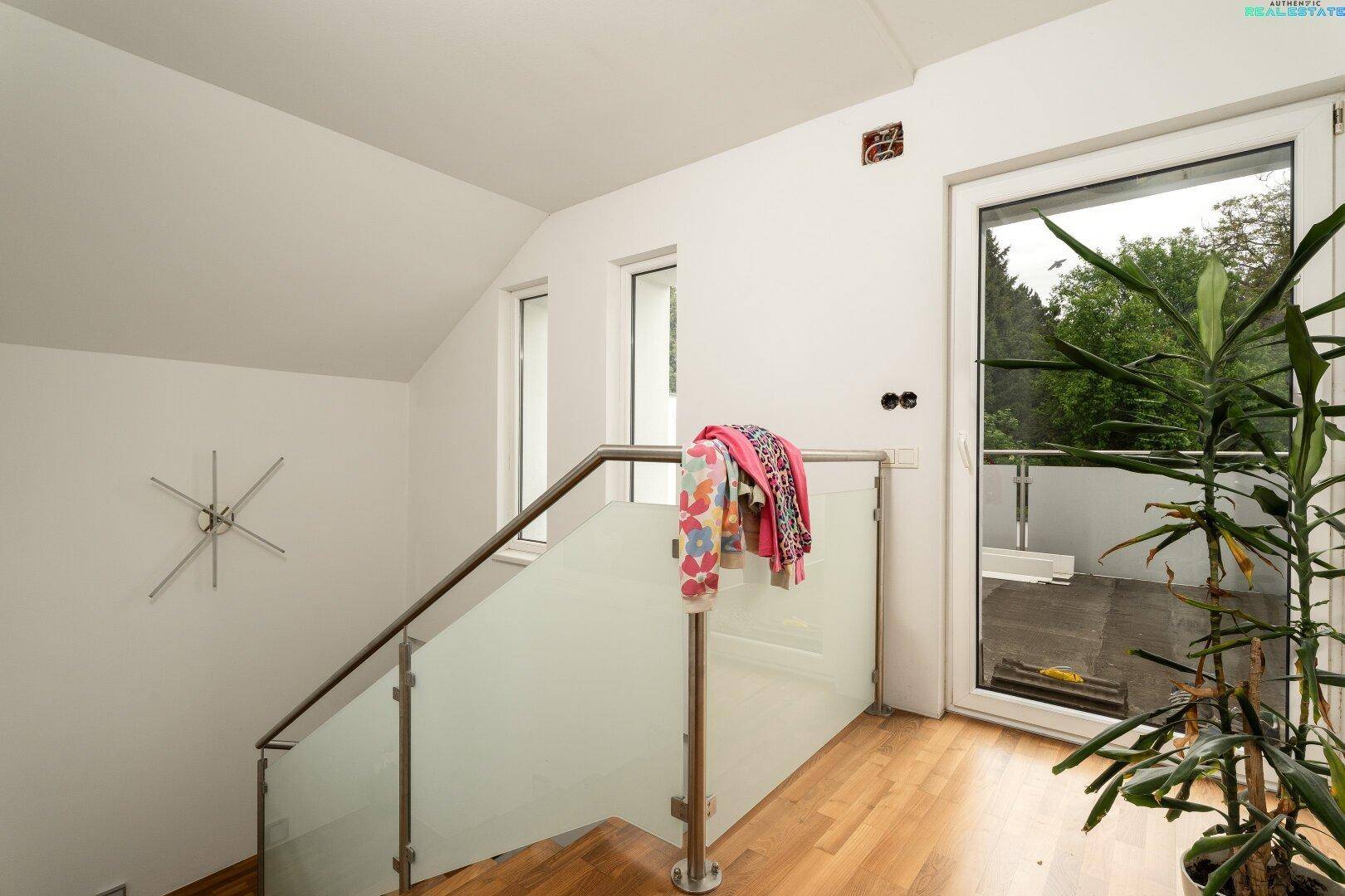 Treppenhaus mit modernem Glasgeländer und Zugang zu einem Außenbereich, sehr stilvoll.