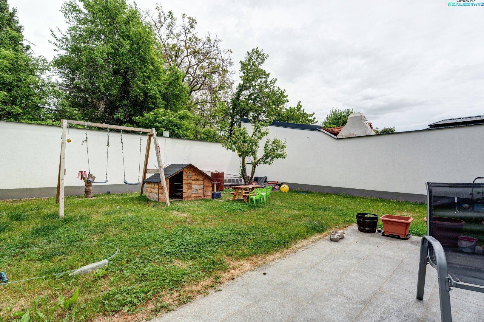 Gartenbereich mit Rasenfläche, Schaukel und kleinem Spielhaus, perfekt für Familien mit Kindern.