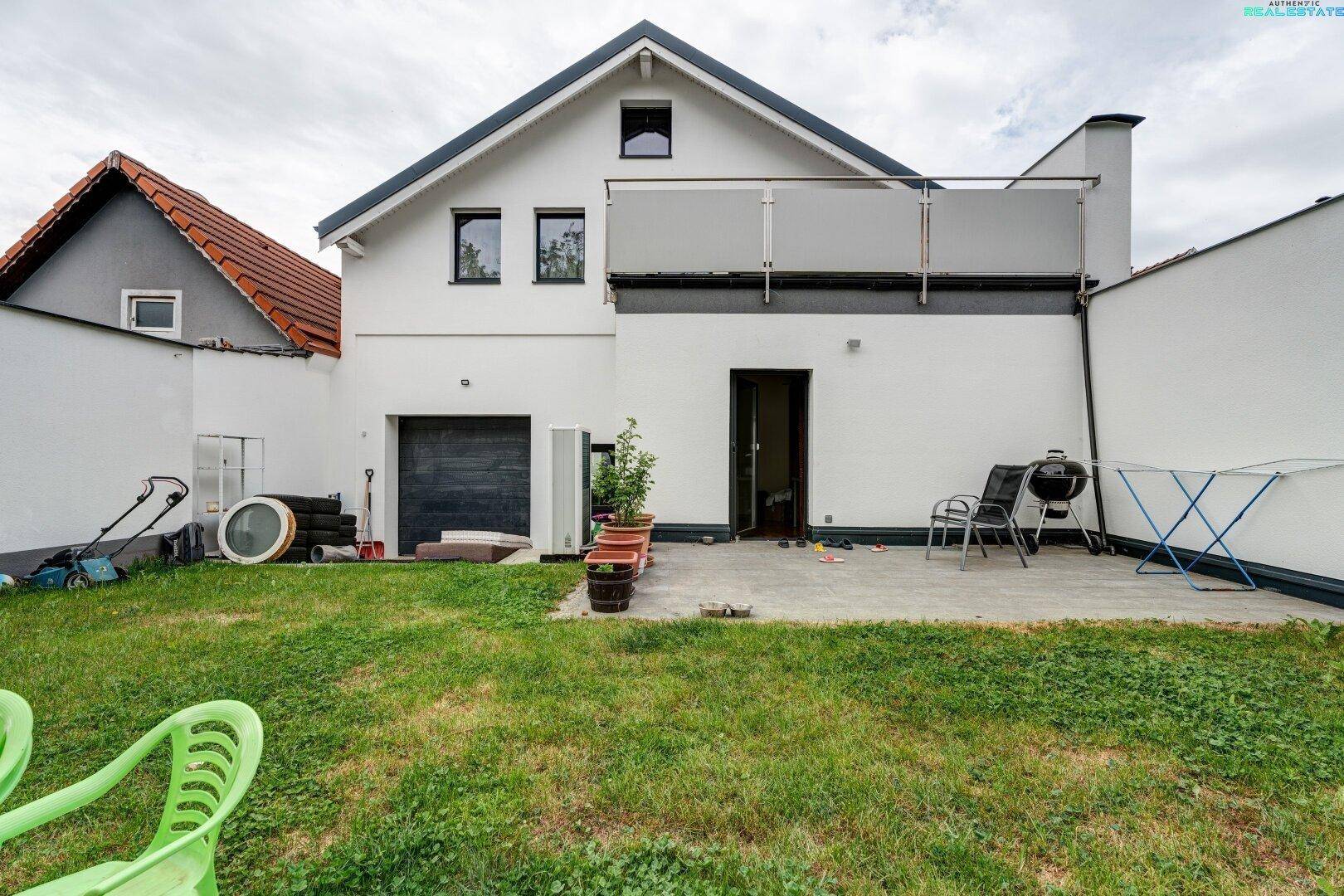 Rückseite des Hauses mit Terrasse, Rasenfläche und Zugang zum Garten, ideal für Grillabende.
