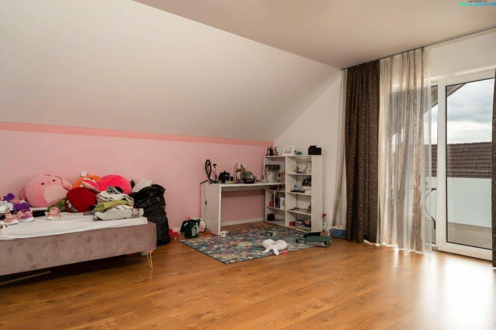 Kinderzimmer im Dachgeschoss mit Holzboden, Schreibtisch und Zugang zum Balkon, hell und freundlich.