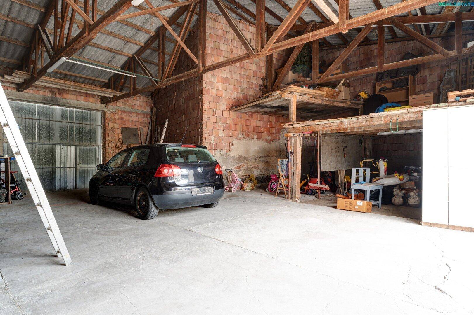 Weitläufige Scheune oder Garage mit Auto, hohen Decken und rustikalen Ziegelwänden.
