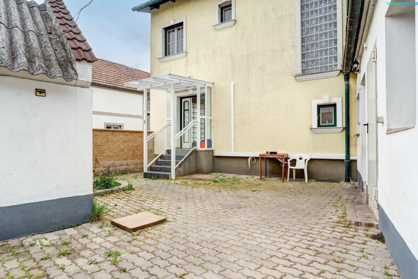 Gelbe Hausfassade mit gepflastertem Hof und überdachtem Eingangsbereich, der zum Haus führt.