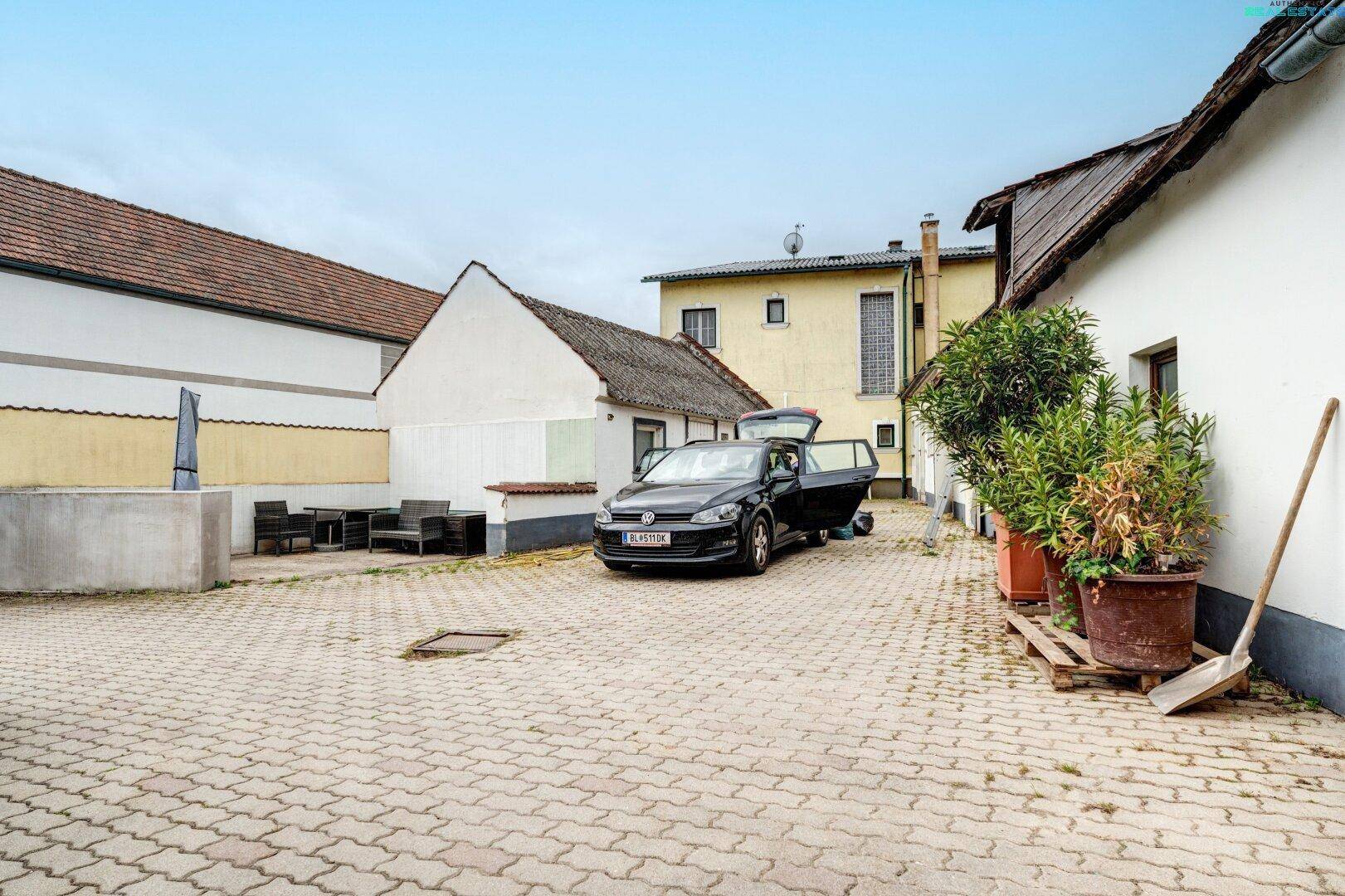 Gepflasterter Innenhof mit geparktem Auto, Topfpflanzen und umliegenden Gebäuden.