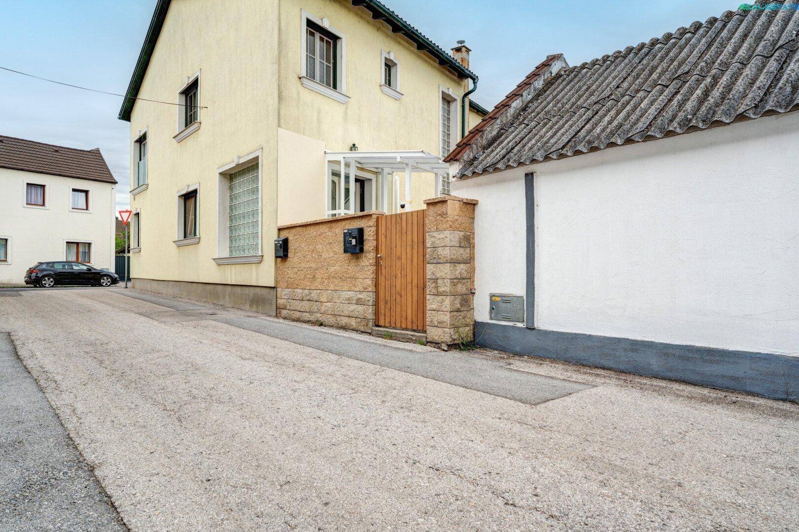 Straßenseite des Hauses mit Eingangsbereich, einer kleinen Steinmauer und einem Holztor.