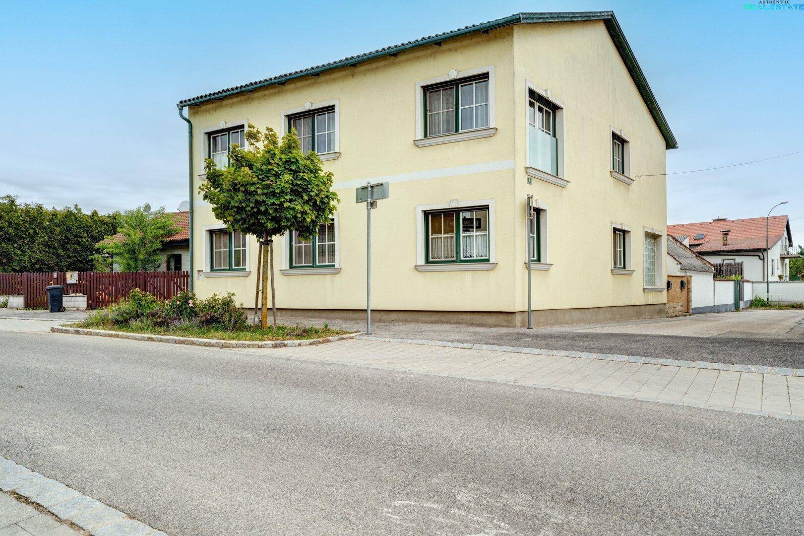 Gelbes Wohnhaus mit grünen Fensterrahmen und Satteldach von der Straßenseite aus gesehen.