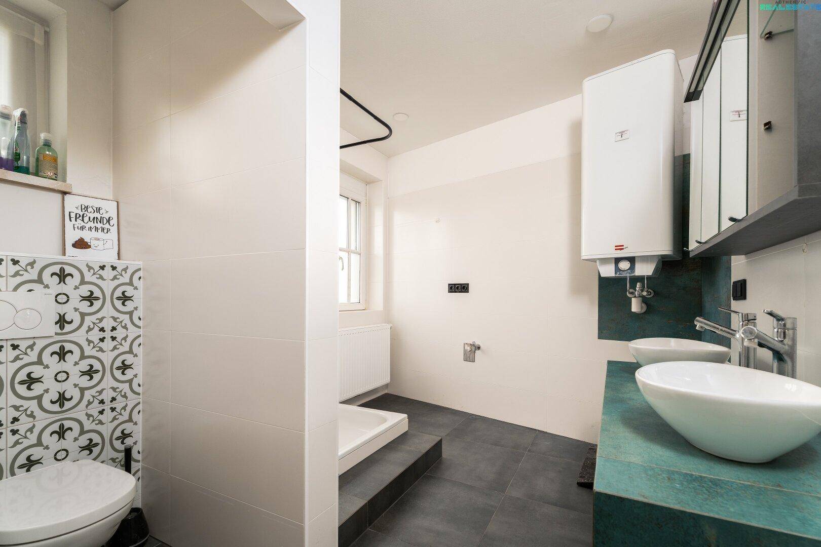 Modernes Badezimmer mit dunklen Fliesen, zwei Aufsatzwaschbecken und einer begehbaren Dusche.