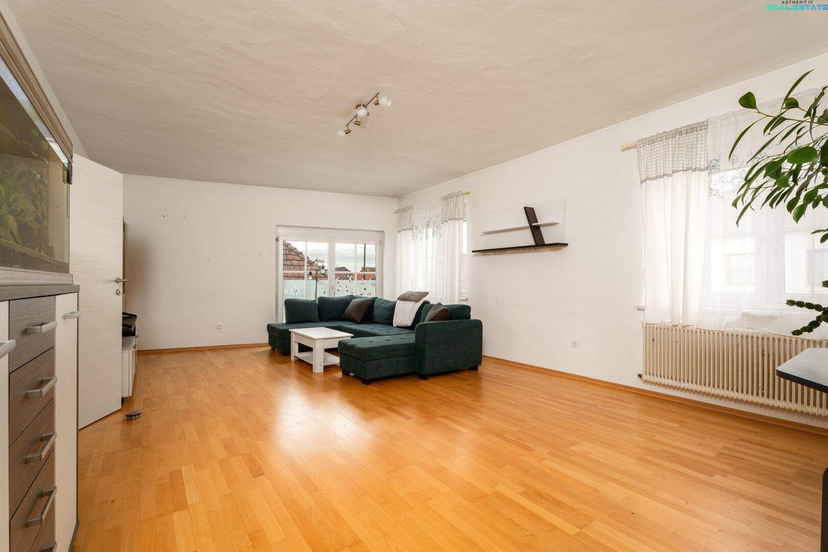 Gemütliches Wohnzimmer mit großem Sofa, Couchtisch, Holzfußboden und hellen Fenstern.