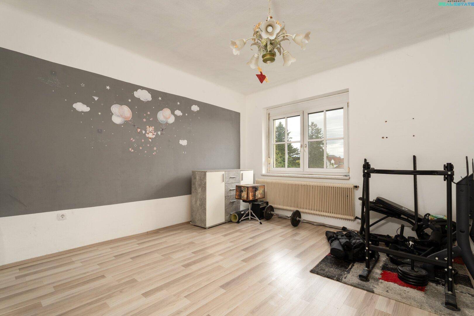 Zimmer mit Laminatboden, Fenster, Heizkörper und einer grauen Akzentwand mit Wolkenmotiven.