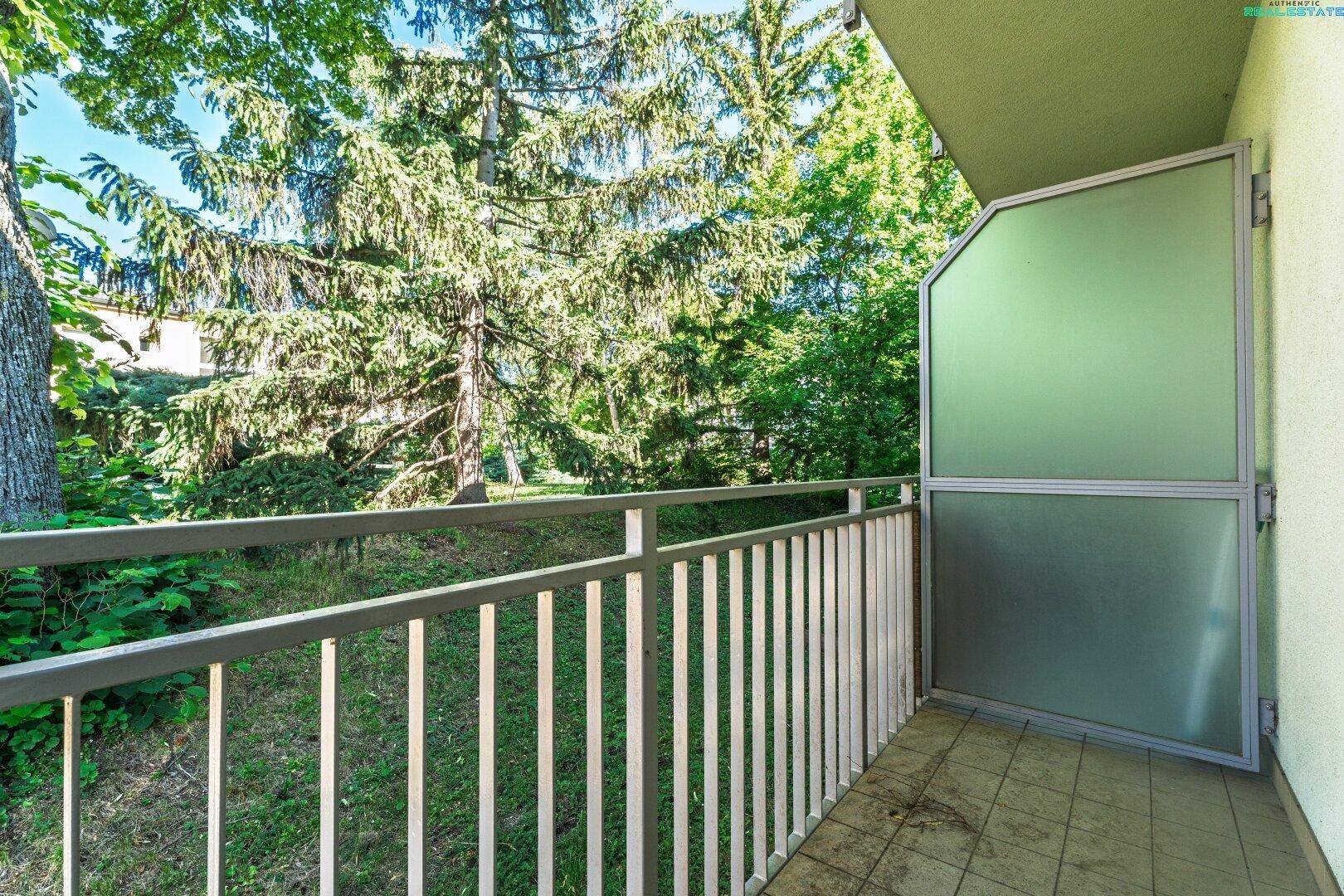 Balkon mit Metallgeländer und Blick ins Grüne mit hohen Bäumen.