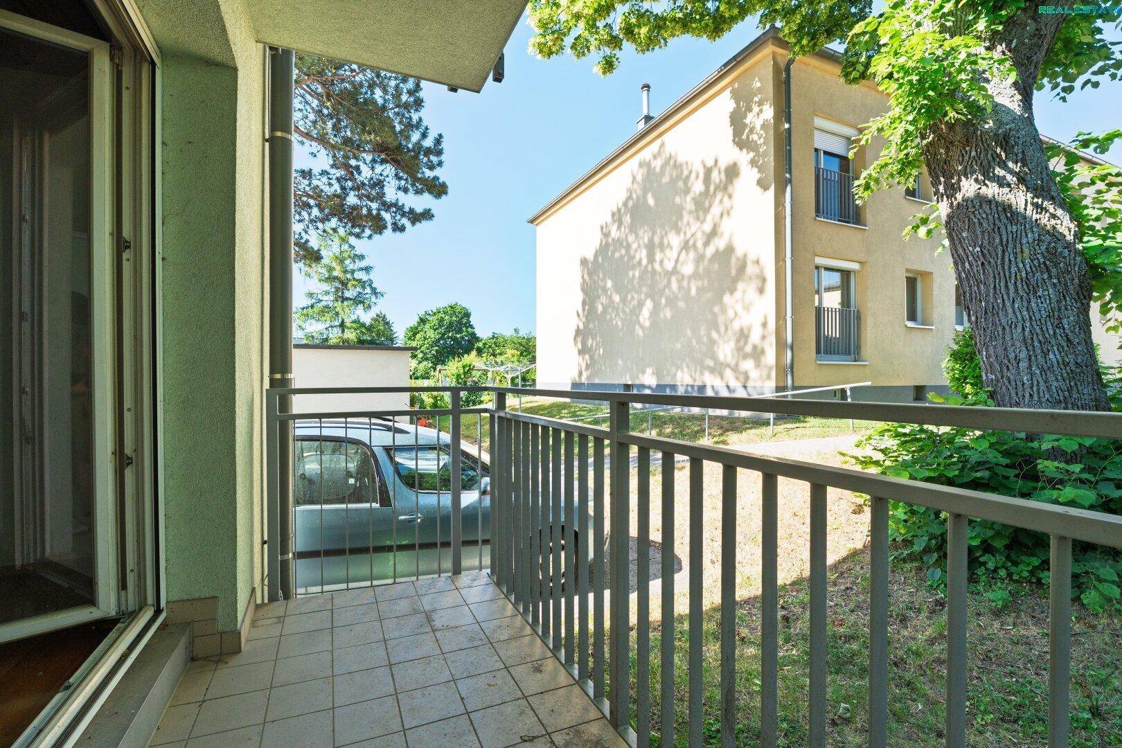 Balkon mit Fliesenboden und Blick auf ein Gebäude sowie Bäume im Hintergrund.