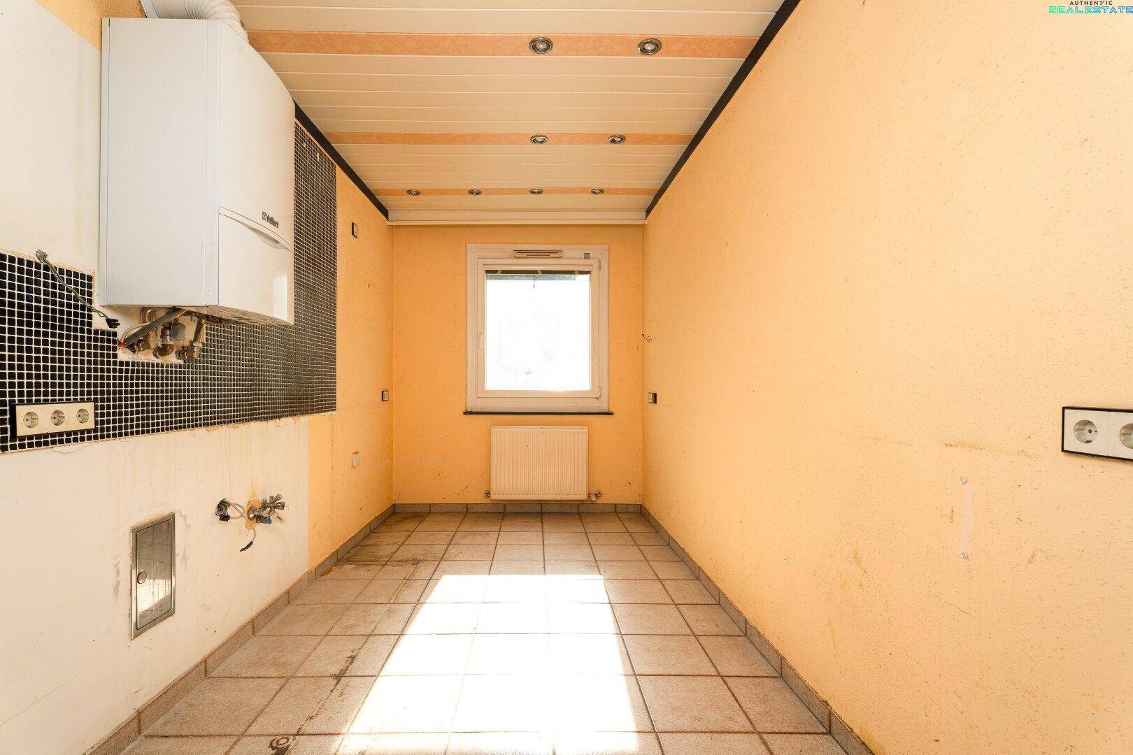 Leere Küche mit gelben Wänden, Fliesenboden und einem Fenster, bereit für die Installation.